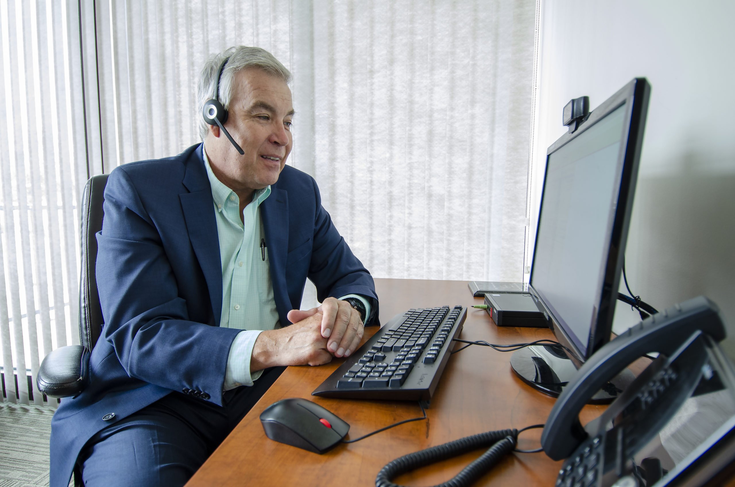 A businessman at his computer takes a call from his headset