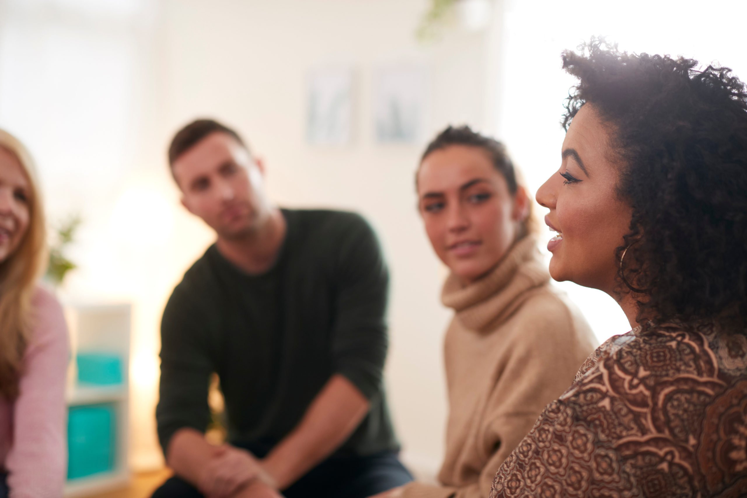 A group listens to a woman while sitting in a circle