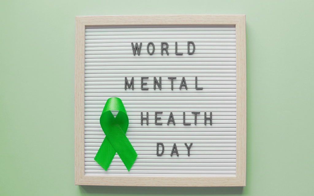 Green background with white sign and green ribbon that reads World Mental Health Day