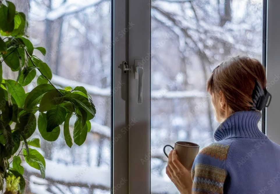 Woman looking out her window during winter while holding a coffee