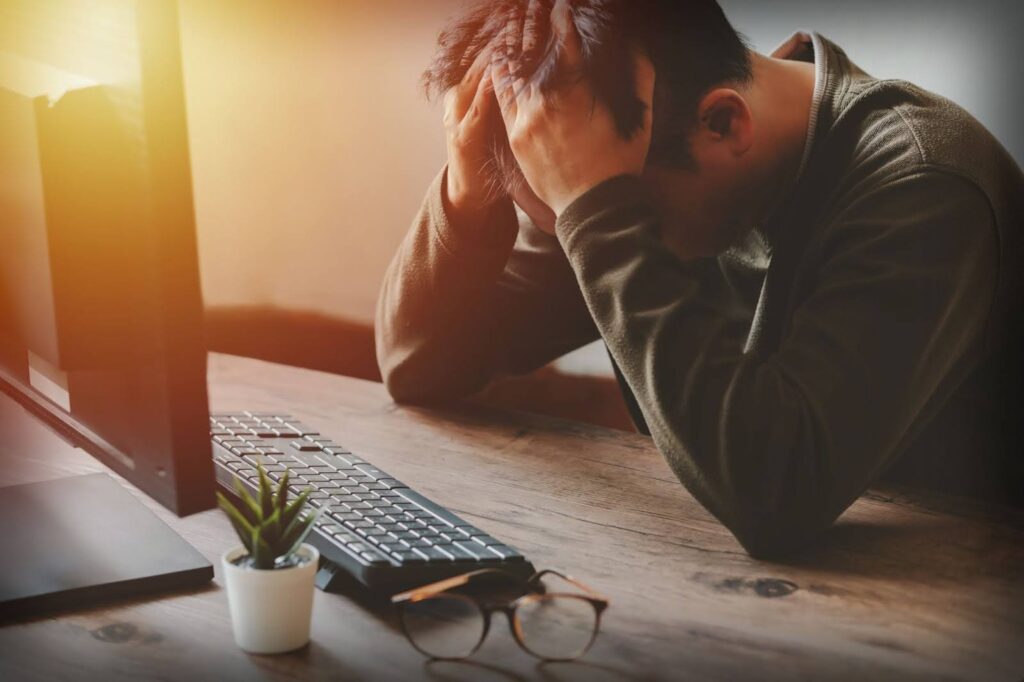 Anxious man at his computer with his head in his hands