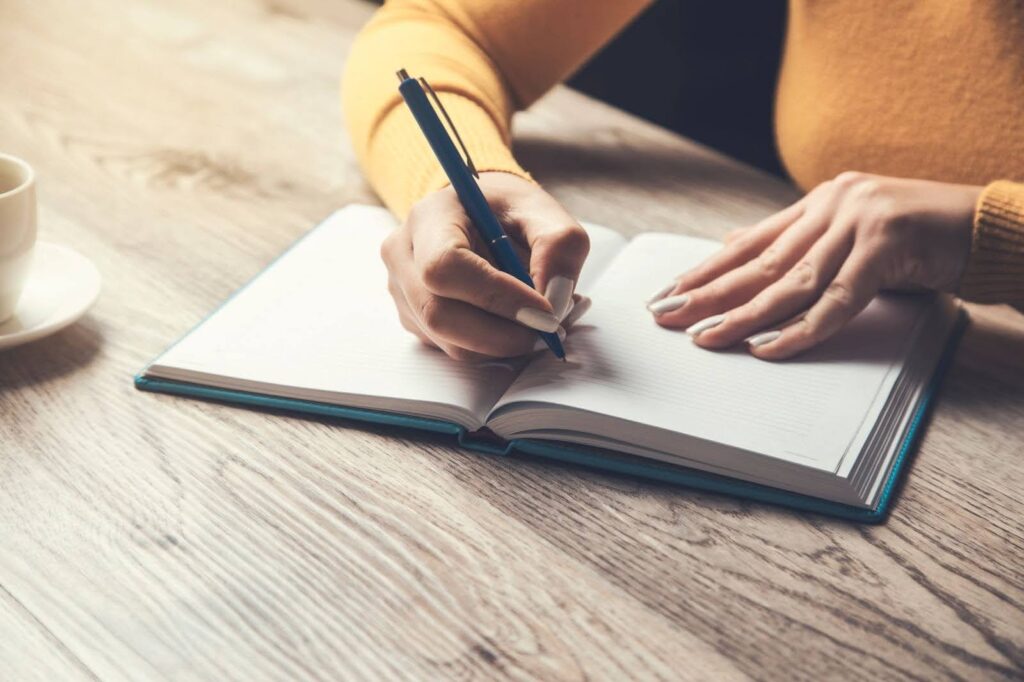 Person writing mental health supporting prompts in their notebook