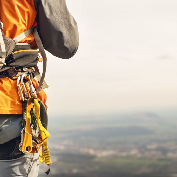 Close-up of a thigh climber with equipment on a belt, stands on a rock on hills background